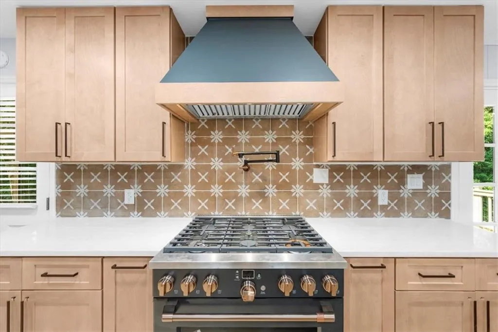 Kitchen with light brown cabinets, wall chimney exhaust hood, range with gas stovetop, and tasteful backsplash