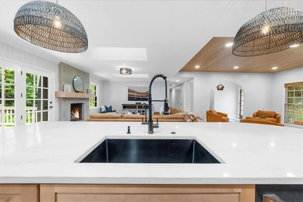 Kitchen with hanging light fixtures, light stone countertops, open floor plan, light brown cabinetry, and a large fireplace
