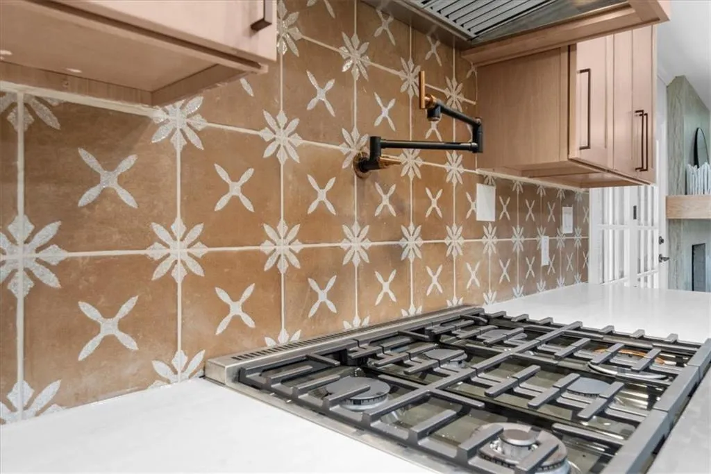 Kitchen view of pot filler, stainless steel gas cooktop, decorative backsplash, custom range hood, and light stone counters