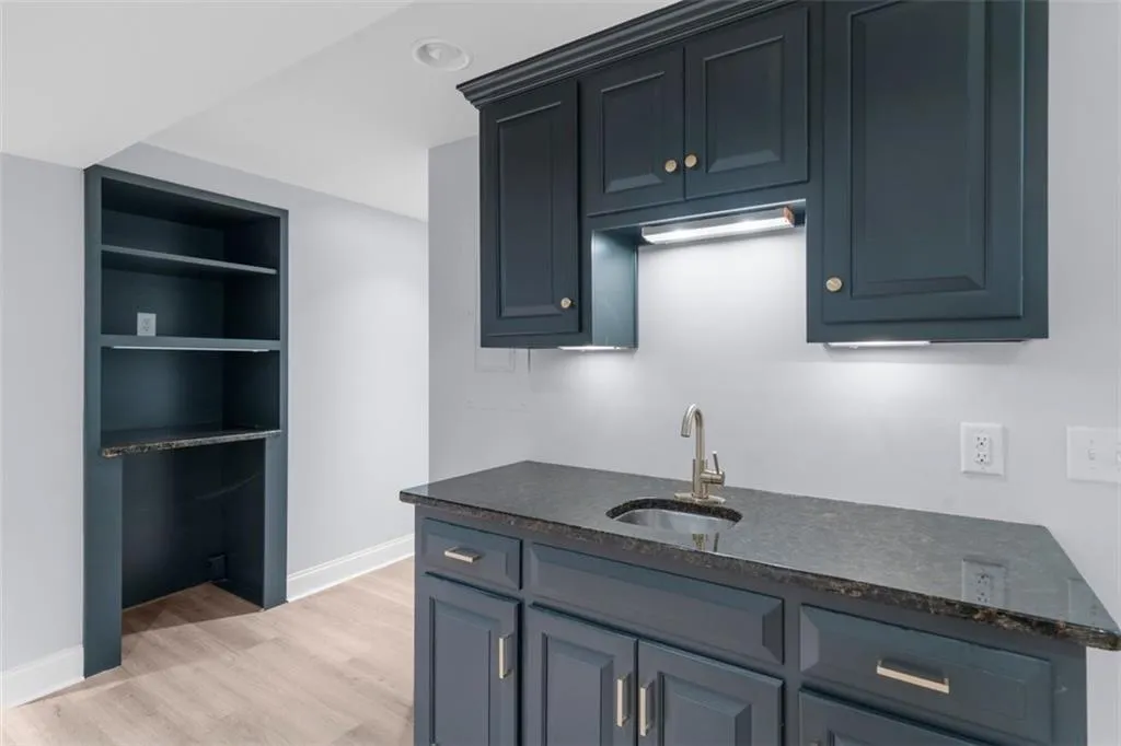 Kitchen with light wood finished floors, dark stone counters, blue cabinetry, and built in shelves
