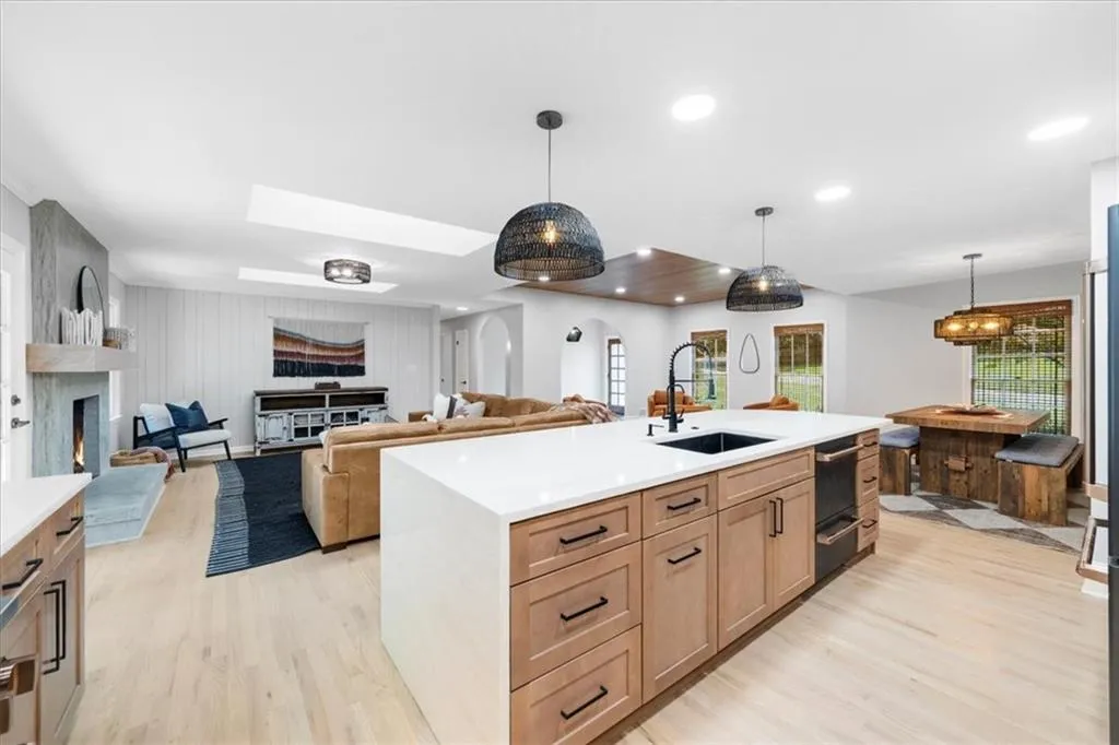 Kitchen featuring open floor plan, a skylight, light wood-style flooring, a large fireplace, and pendant lighting