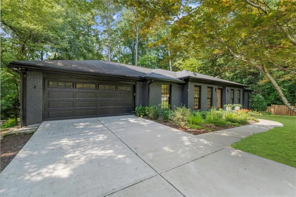 View of front of house with brick siding, an attached garage, driveway, and view of scattered trees
