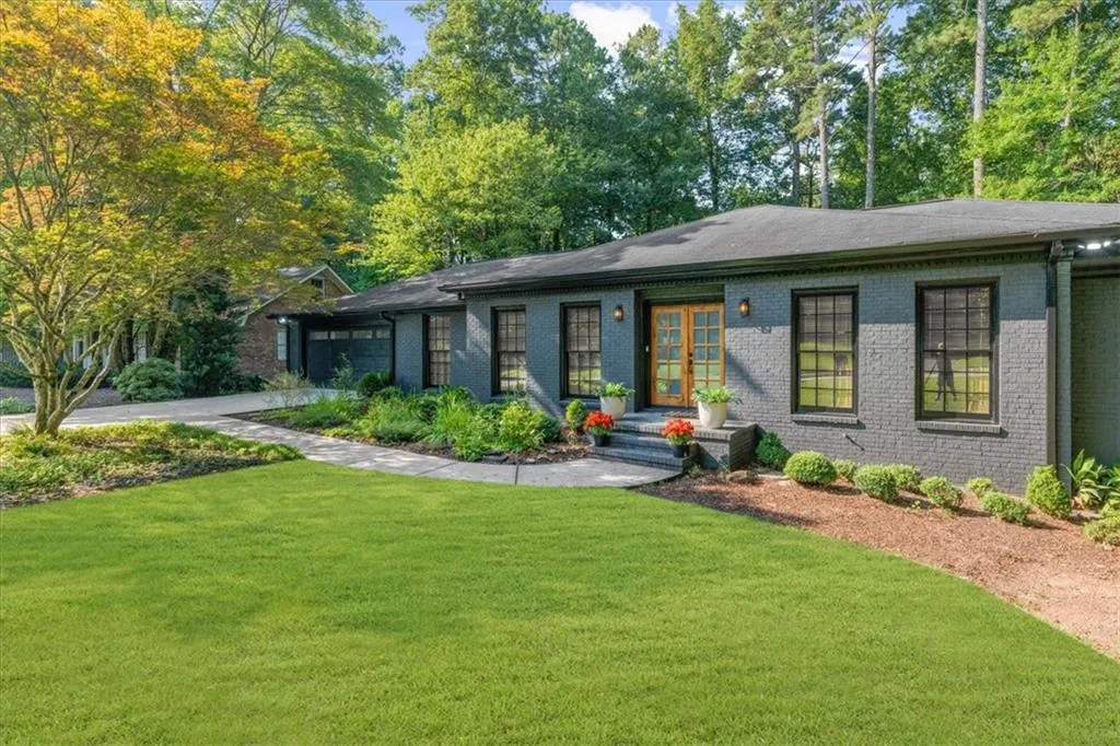 Ranch-style house with a front yard, brick siding, an attached garage, and view of scattered trees