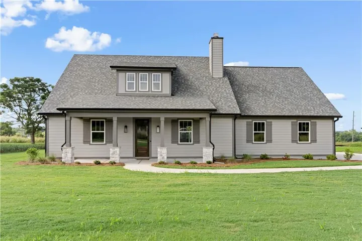 Light gray exterior siding with dark gray shutters, front porch with stone-clad columns, dark wood-finish front door, and an architectural shingle roof