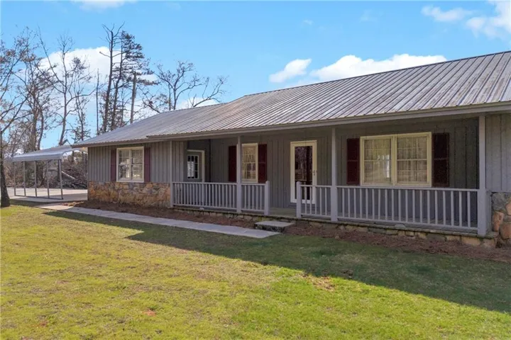View of front of home featuring covered porch, board and batten siding, stone siding, and a front lawn