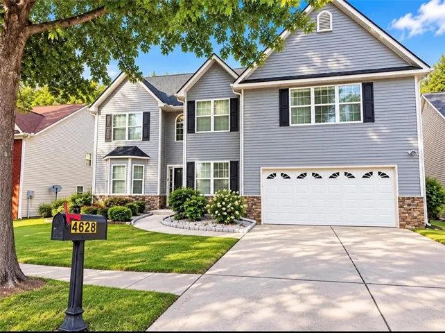 Two-story home with light gray siding, black window shutters, and a stone veneer foundation
