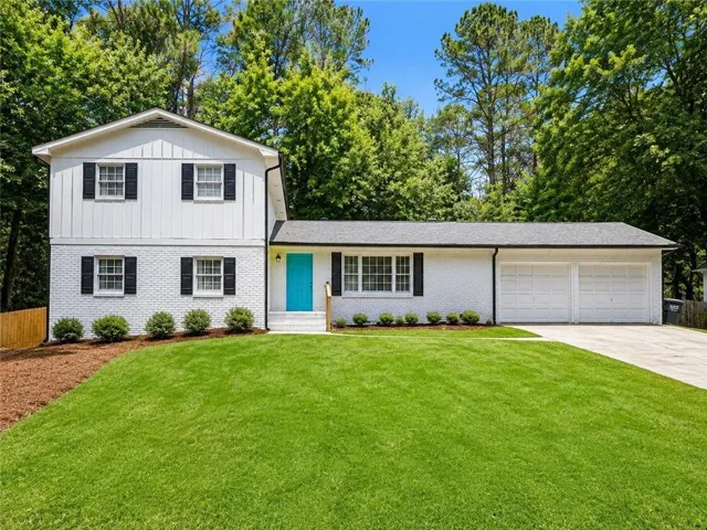 White brick and vertical siding exterior with a vibrant teal front door, black shutters, and a two-car garage