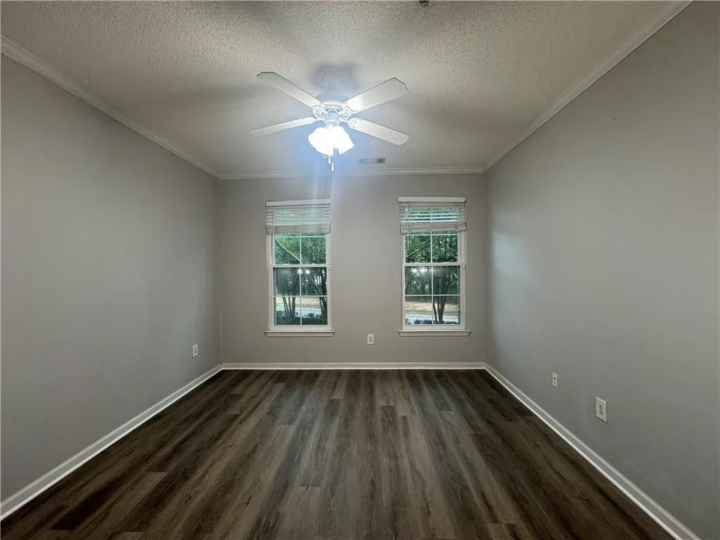 Unfurnished room featuring a textured ceiling, ornamental molding, dark wood-type flooring, and ceiling fan