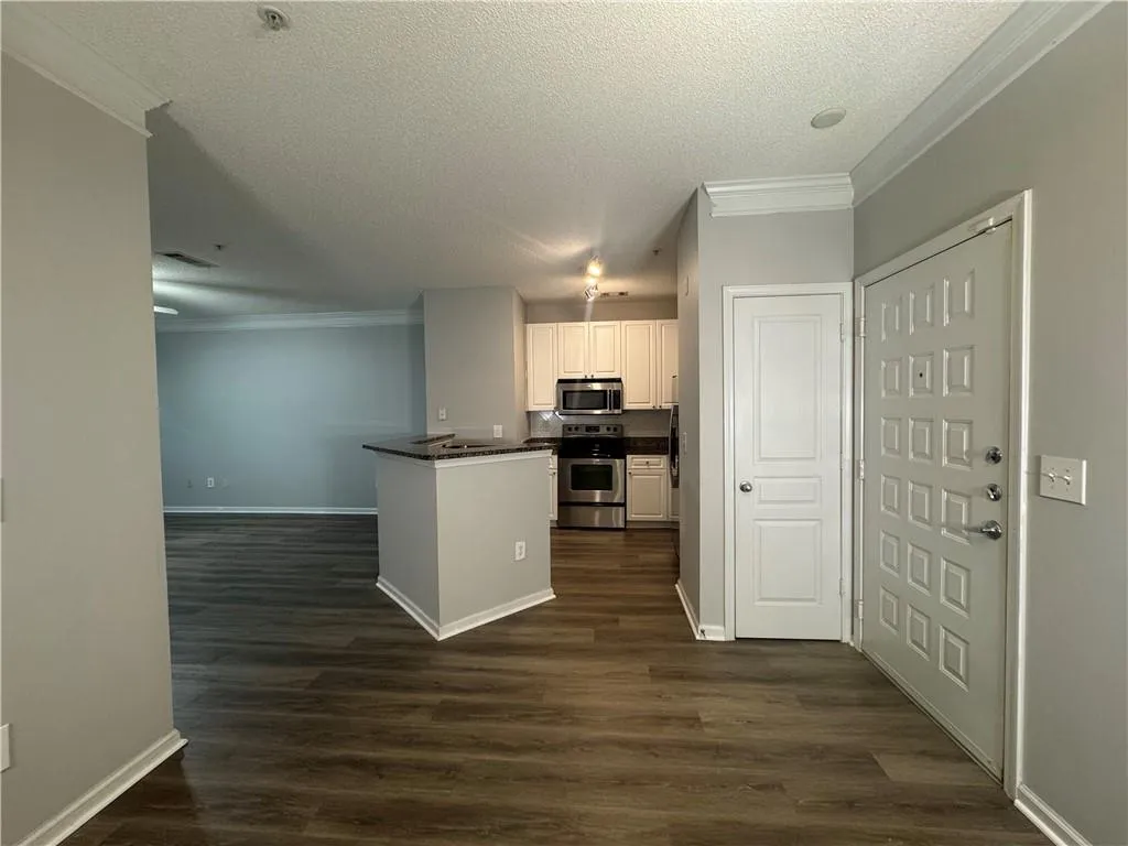 Kitchen with ornamental molding, a textured ceiling, dark countertops, appliances with stainless steel finishes, and dark wood-type flooring