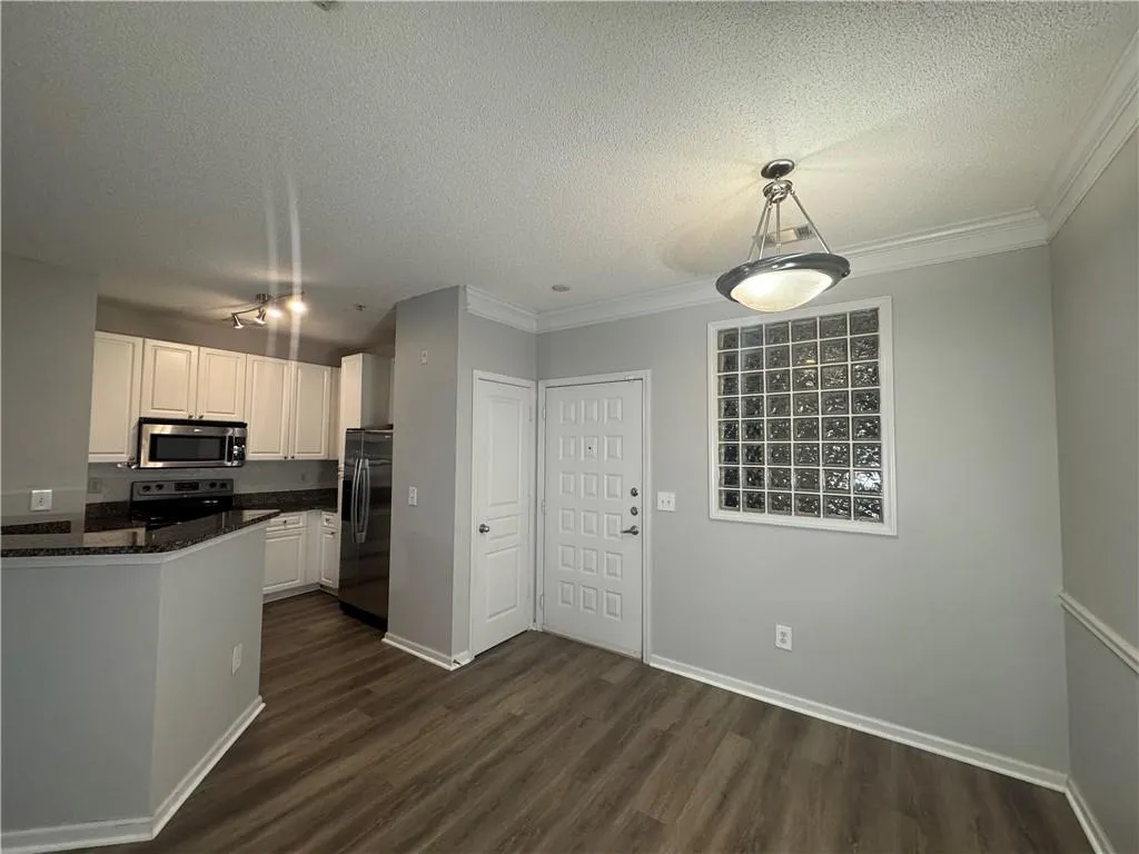 Kitchen with a textured ceiling, dark wood finished floors, white cabinetry, appliances with stainless steel finishes, and decorative light fixtures