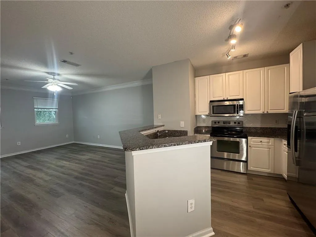 Kitchen with appliances with stainless steel finishes, a textured ceiling, dark wood-style flooring, tasteful backsplash, and white cabinets