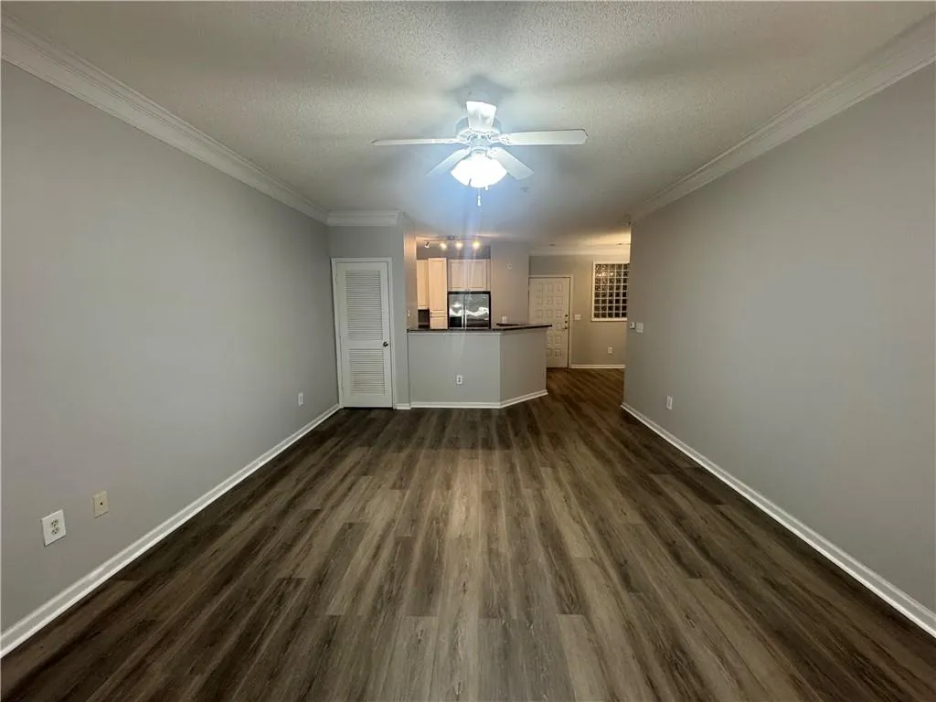 Unfurnished living room featuring a textured ceiling, dark wood finished floors, and crown molding