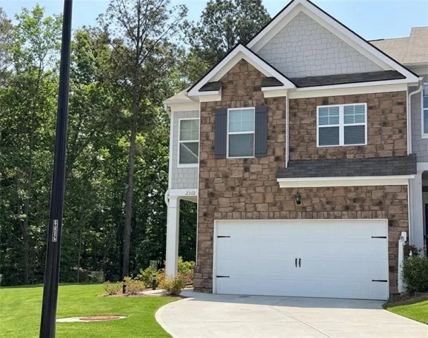 View of front of property with stone siding, a garage, concrete driveway, a front yard, and roof with shingles