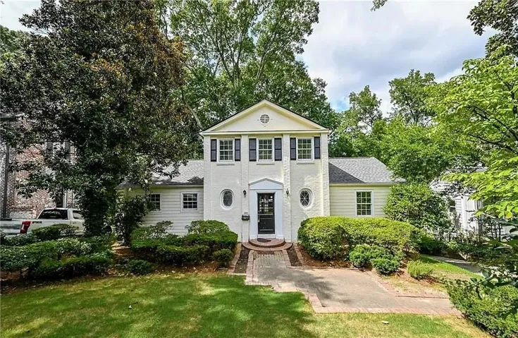 Traditional-style residence featuring a prominent front gable, white brick facade, dark shutters, and a brick walkway