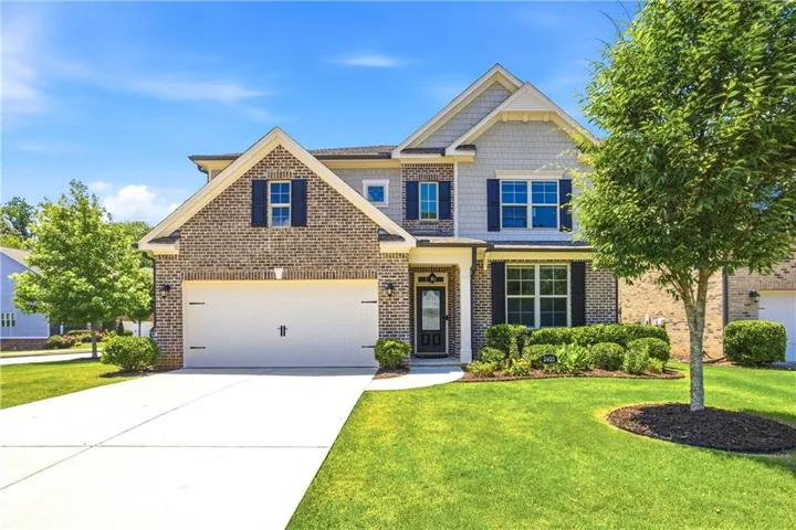 Brick and siding exterior featuring a two-car garage, manicured lawn, established landscaping, a concrete driveway, and an arched entry with a glass-paneled door