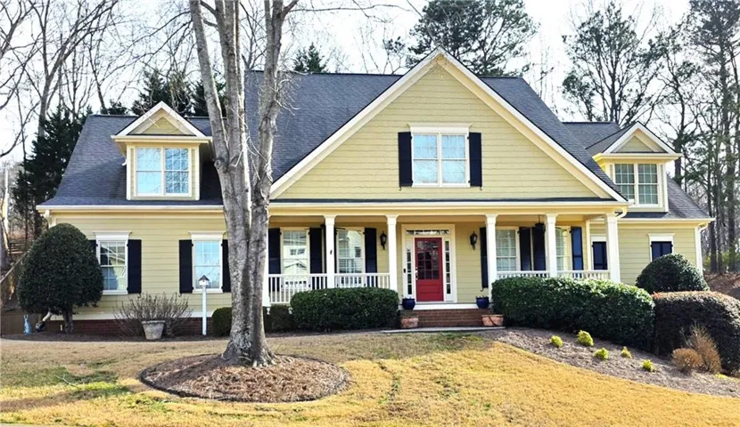 Gabled roofline with dormer windows, yellow siding, red entry door, white columned porch, and dark shutters