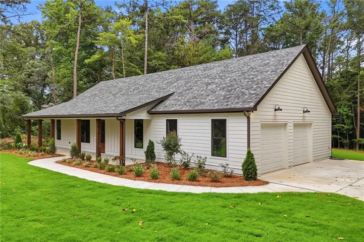 White siding exterior with a dark shingle roof, featuring a covered front porch with dark wood columns, a two-car garage, and a concrete driveway