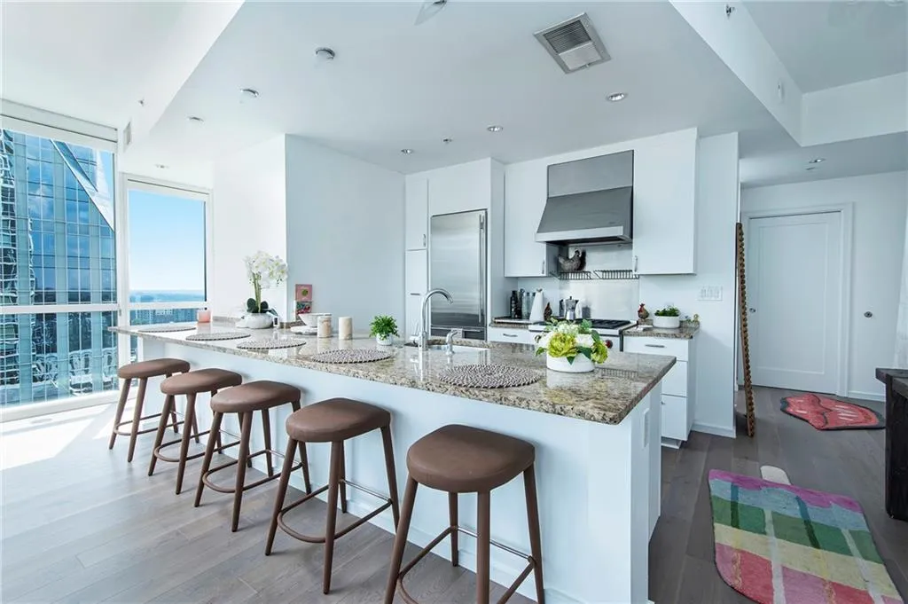 Kitchen featuring a kitchen bar, white cabinetry, dark wood-type flooring, light stone counters, and a wall of windows