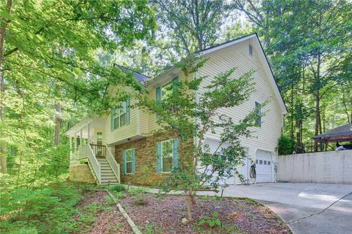 Exterior featuring two-car garage, stone façade, light-colored siding, and a covered front porch with steps and railing