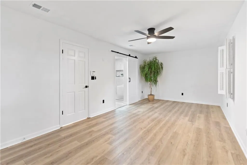 Spare room with a barn door, ceiling fan, and light wood-style floors