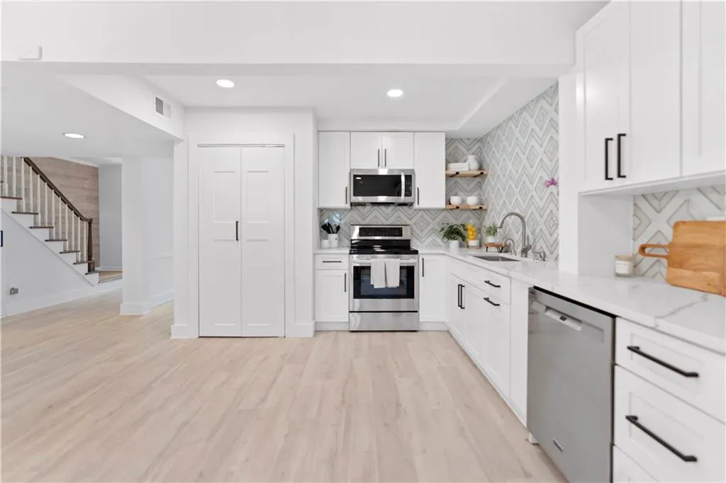 Kitchen with appliances with stainless steel finishes, open shelves, tasteful backsplash, white cabinets, and light wood-type flooring