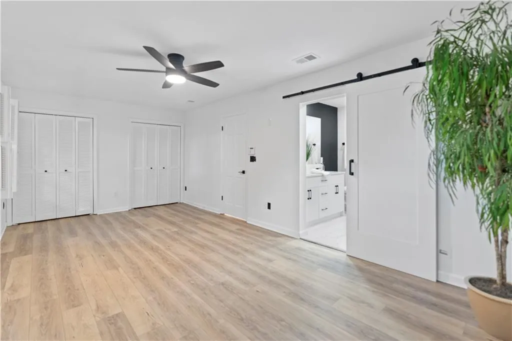 Unfurnished bedroom featuring a barn door, light wood-type flooring, two closets, ensuite bathroom, and a ceiling fan