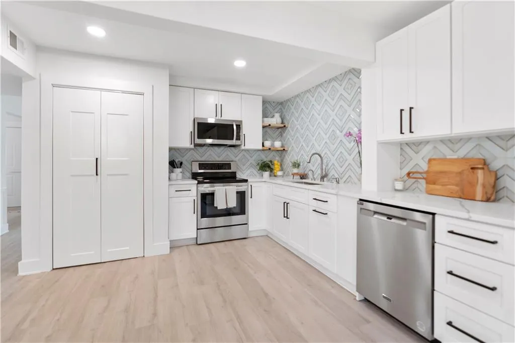 Kitchen featuring stainless steel appliances, light wood-type flooring, open shelves, tasteful backsplash, and white cabinetry