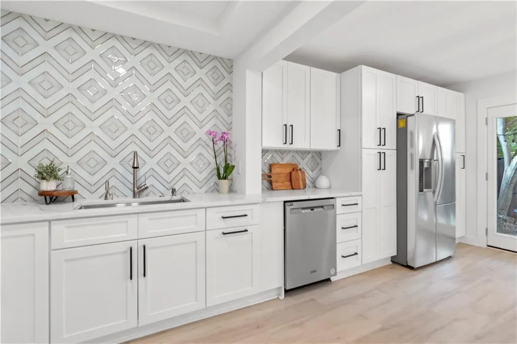 Kitchen with stainless steel appliances, backsplash, light wood-style floors, and white cabinets
