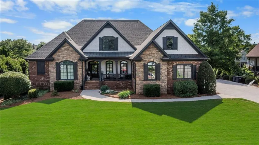 Stone and brick-clad residence featuring a covered front porch with dark columns, dark window shutters, and a prominent gable roofline