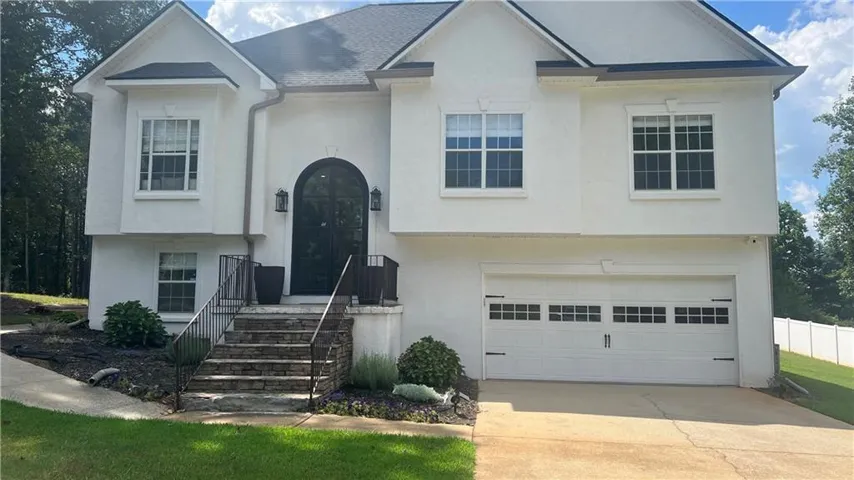 Stucco exterior with an arched entryway, stone-clad steps, black metal handrails, and a two-car garage with decorative hardware
