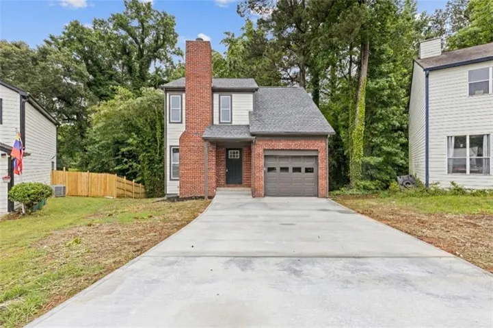 Charming brick Colonial with a freshly poured concrete driveway, attached one-car garage, and mature landscaping