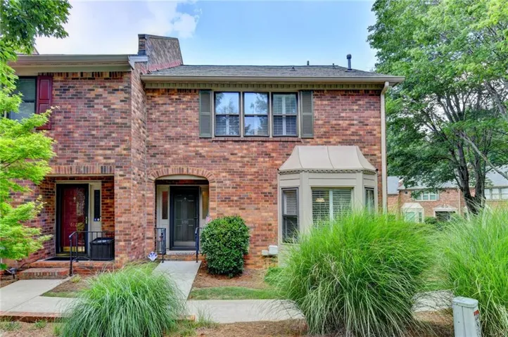 Brick townhouse exterior featuring a covered bay window, arched entryways, and mature landscaping
