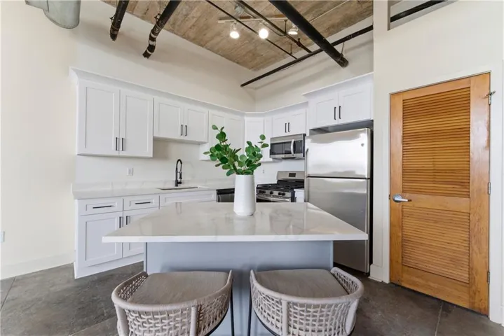 Kitchen featuring stainless steel appliances, light stone countertops, white cabinets, a kitchen island, and a kitchen bar