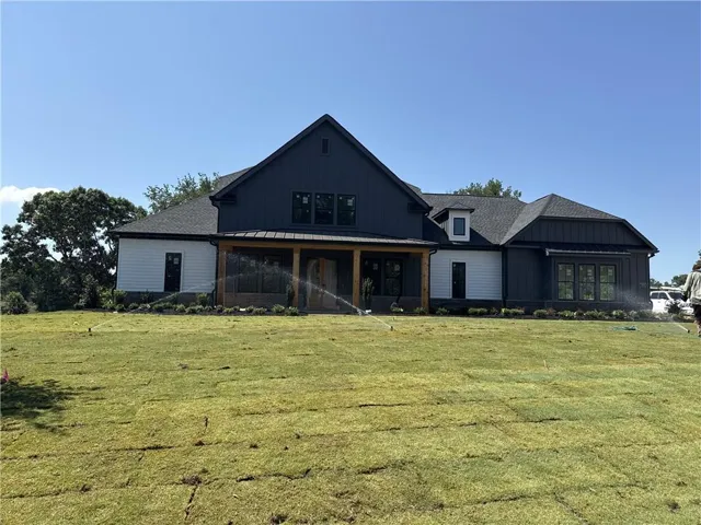 Dark-hued board and batten siding with white horizontal siding accents, multiple windows, a covered patio with wood columns, and a dormer window