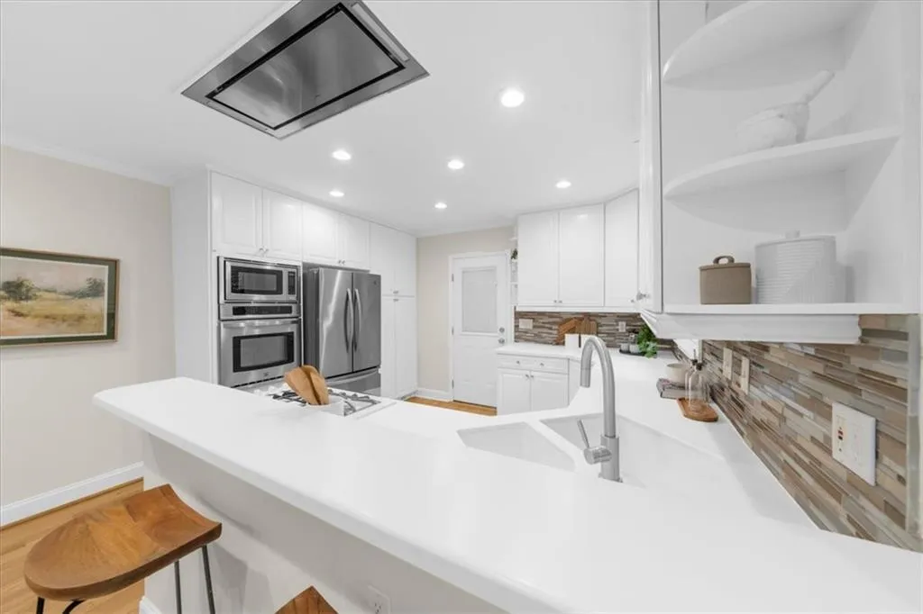 Kitchen with open shelves, decorative backsplash, white cabinets, exhaust hood, and light countertops