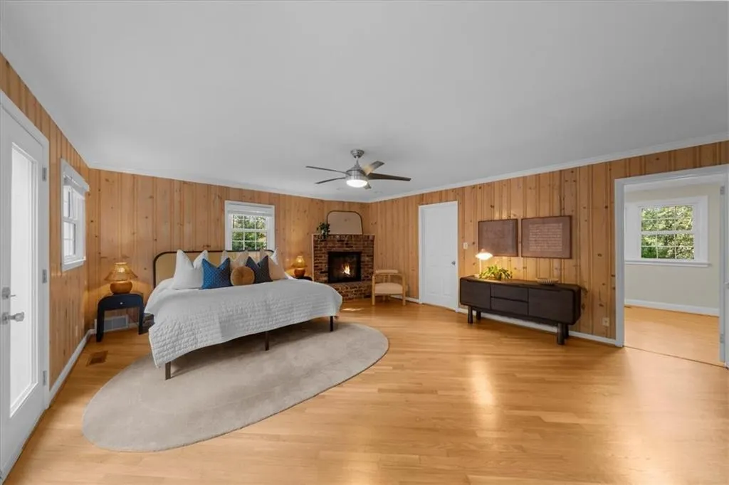 Bedroom with wood walls, a ceiling fan, light wood-style floors, crown molding, and a brick fireplace
