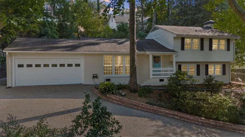 Split level home with a chimney, decorative driveway, brick siding, covered porch, and a garage
