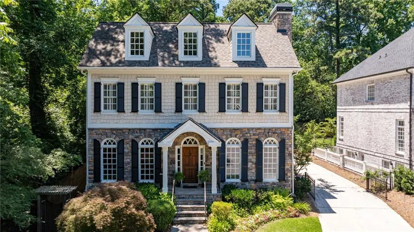 Traditional-style residence featuring a stone and shingle facade, multiple dormer windows, and a prominent front entrance with a wooden door and arched transom