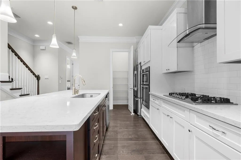 Kitchen with light stone counters, white cabinetry, wall chimney range hood, decorative backsplash, and pendant lighting