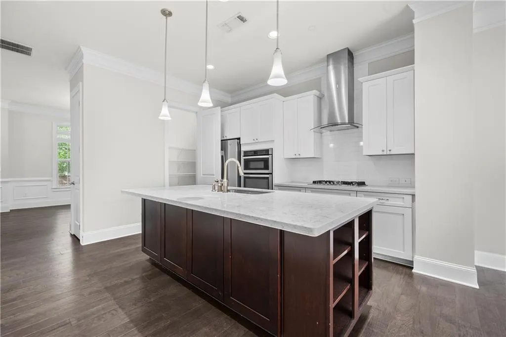 Kitchen featuring crown molding, backsplash, light stone counters, an island with sink, and dark brown cabinetry