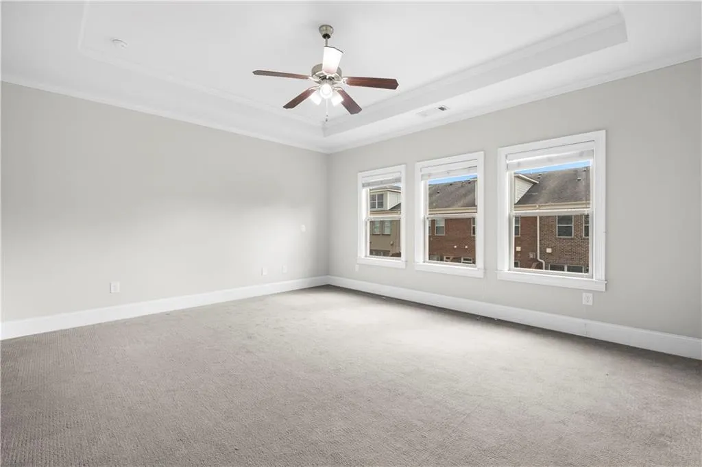 Carpeted spare room featuring a raised ceiling, crown molding, and ceiling fan