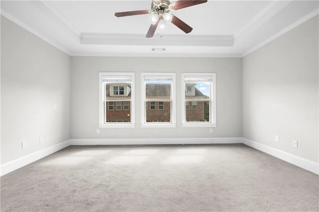 Spare room with a tray ceiling, light colored carpet, crown molding, and ceiling fan