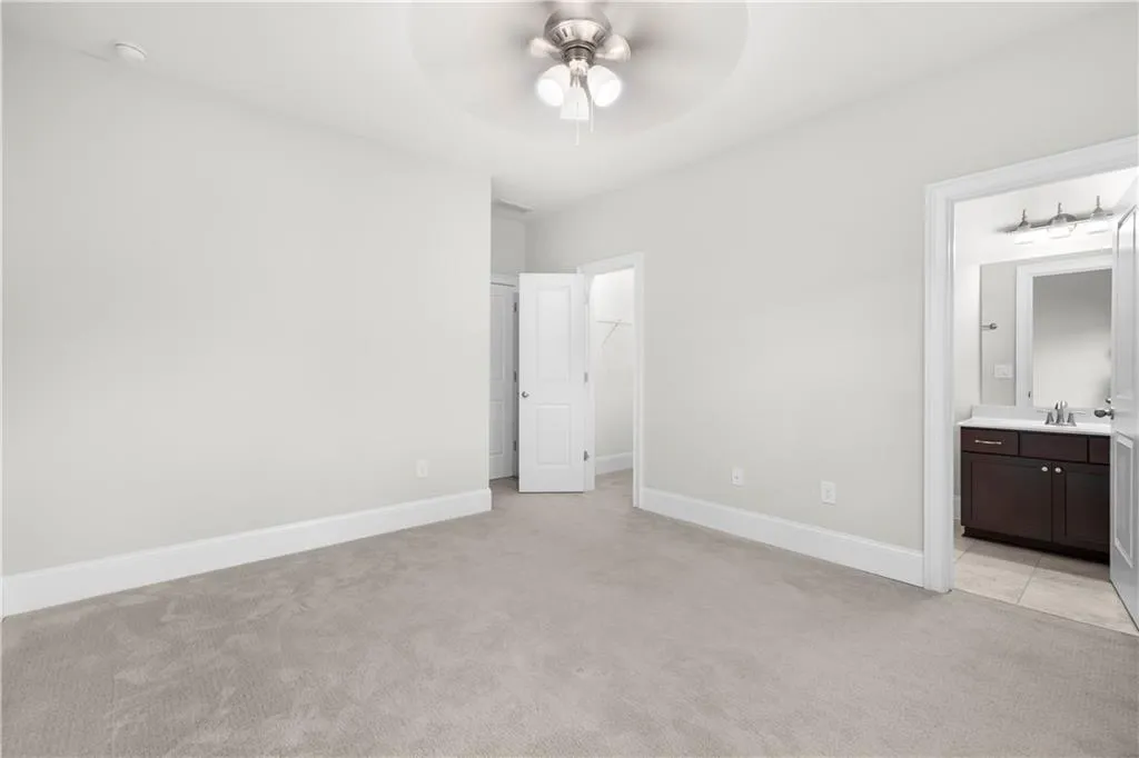 Unfurnished bedroom with ensuite bath, light colored carpet, a walk in closet, and ceiling fan