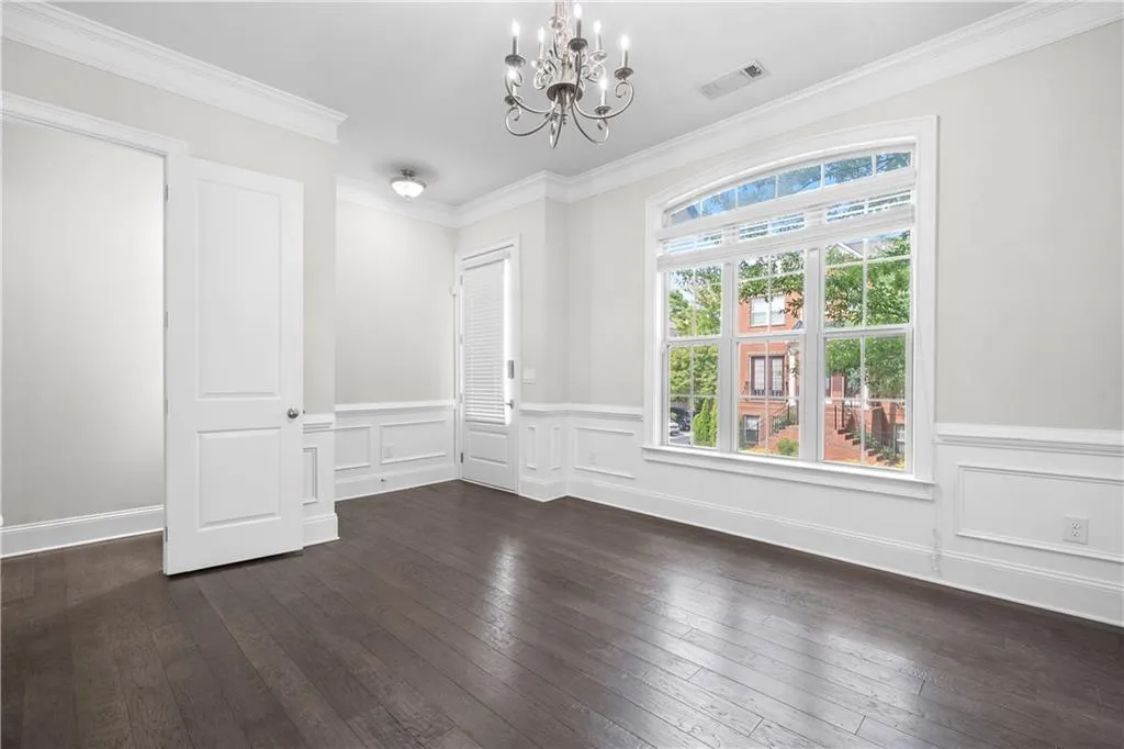 Unfurnished dining area featuring a chandelier, ornamental molding, dark wood finished floors, and wainscoting