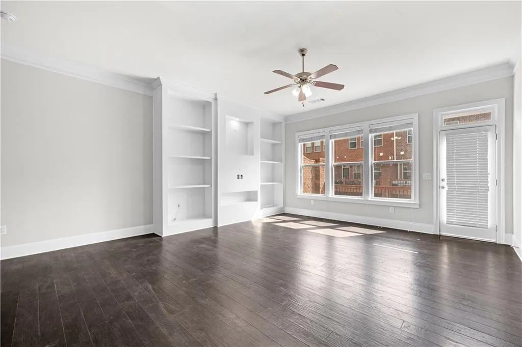 Unfurnished living room featuring ornamental molding, built in shelves, dark wood-style floors, and ceiling fan