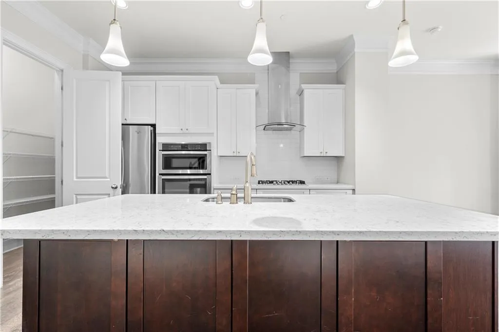 Kitchen featuring white cabinetry, ornamental molding, light stone countertops, tasteful backsplash, and a kitchen island with sink
