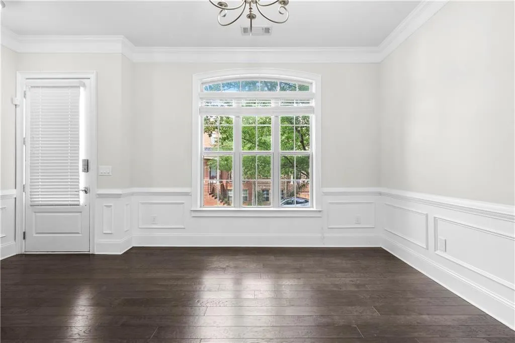 Unfurnished dining area with a chandelier, ornamental molding, dark wood-type flooring, and a wainscoted wall