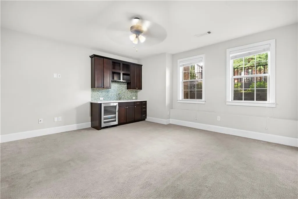 Kitchen featuring dark brown cabinetry, decorative backsplash, light countertops, light carpet, and beverage cooler