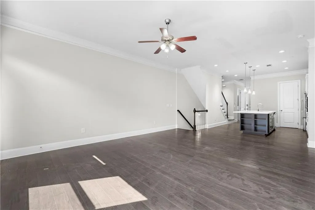 Unfurnished living room featuring ornamental molding, dark wood-style flooring, recessed lighting, ceiling fan, and stairway