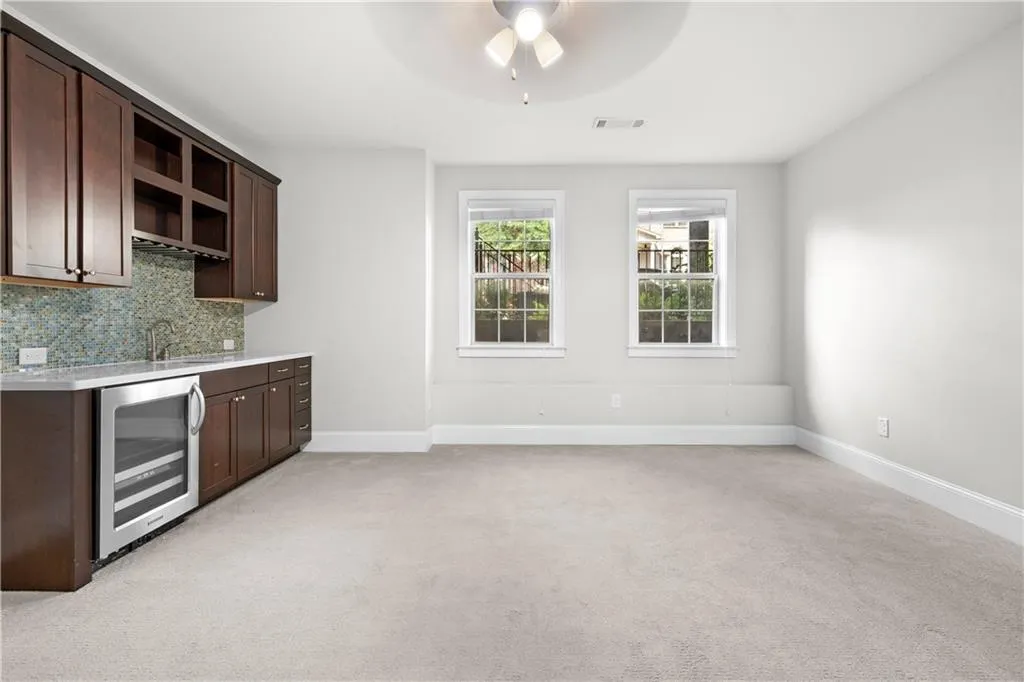 Bar featuring dark brown cabinetry, backsplash, beverage cooler, open shelves, and light colored carpet